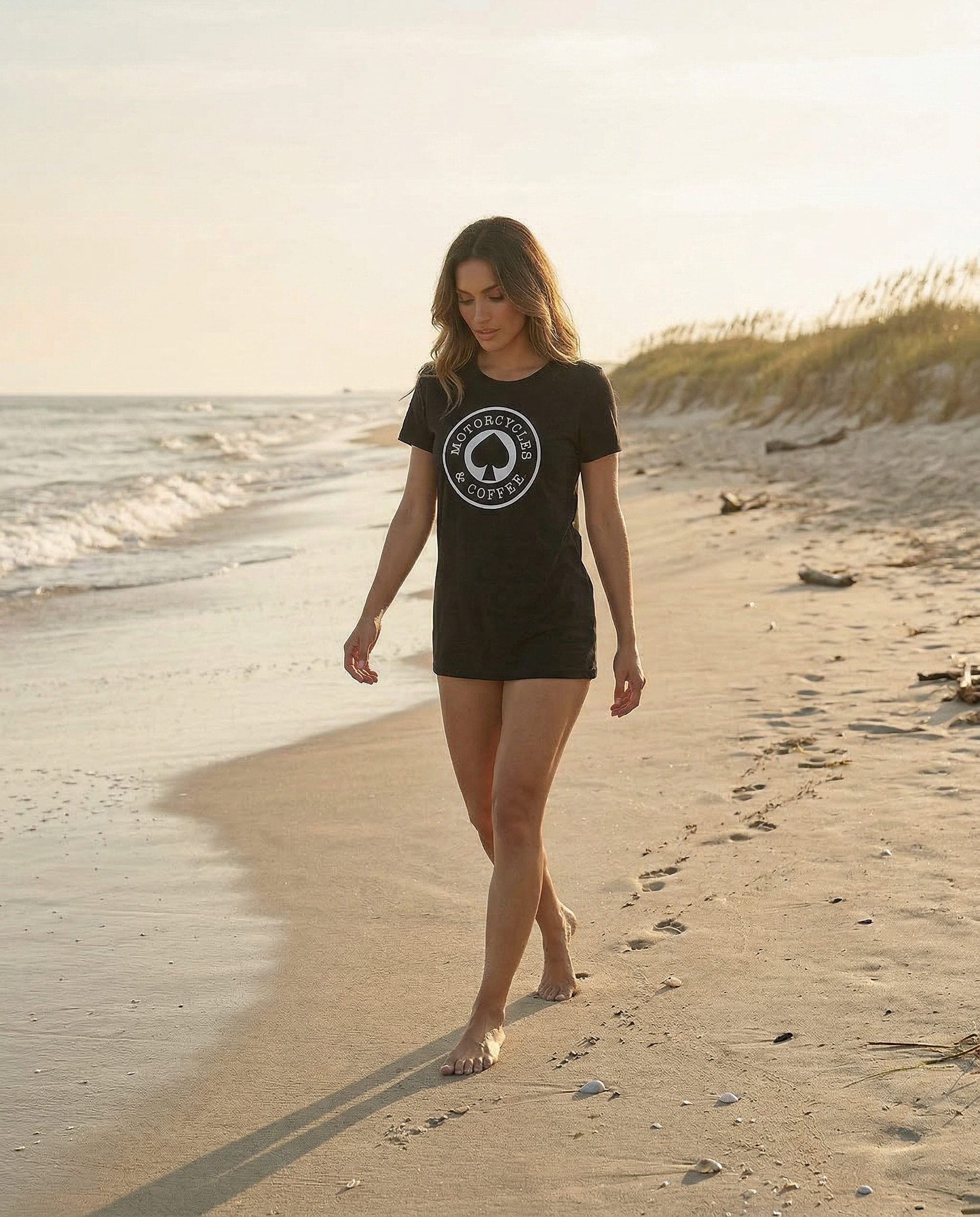 Stylish women’s motorcycle lifestyle apparel featuring the Motorcycles & Coffee Ace tee in a coastal setting.